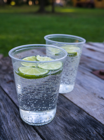 water with lime in a plastic cup on wooden tableの写真素材