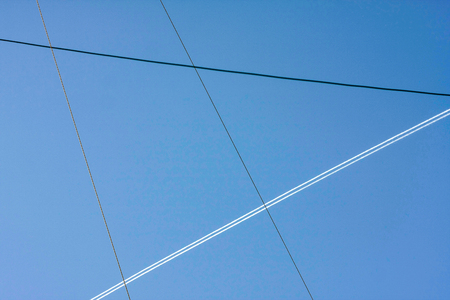 Diagonal powerlines and air track in blue sky at sunny dayの写真素材