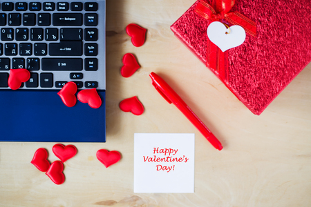 Empty white sticker, pc, red pen, gift box decorated by red hearts on wooden table in office. Happy Valentine's day concept. Copyspace. Place for your text.の写真素材