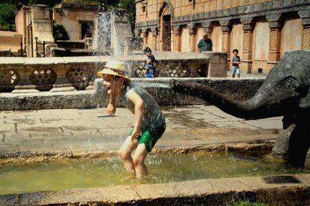 Happy boy with a hat in pool in front of te statue of elephant squirting water out of the trunk on the boy. Hannover Zoo.の写真素材