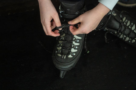 Hands of teenage boy tying a shoestring on an ice skates on the black backgroundの写真素材