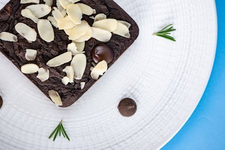 Chocolate Brownie with almond slice in white plate set on light blue background.の写真素材