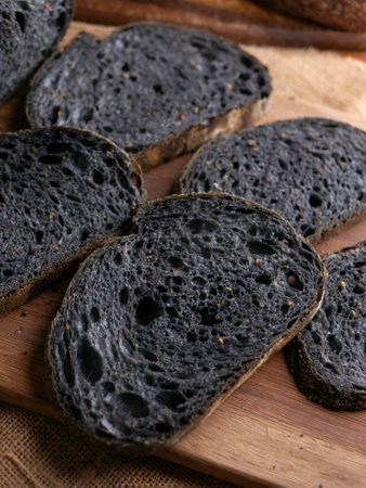 Fresh baked black charcoal sourdough ciabatta bread sliced on wooden boardの写真素材