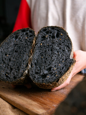 Baker Hand Presenting Homemade fresh baked black charcoal sourdough bread. Showing crumb inside