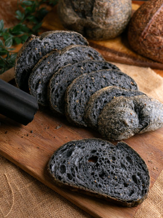 Fresh baked black charcoal sourdough ciabatta bread sliced on wooden boardの写真素材