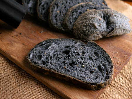 Fresh baked black charcoal sourdough ciabatta bread sliced on wooden board