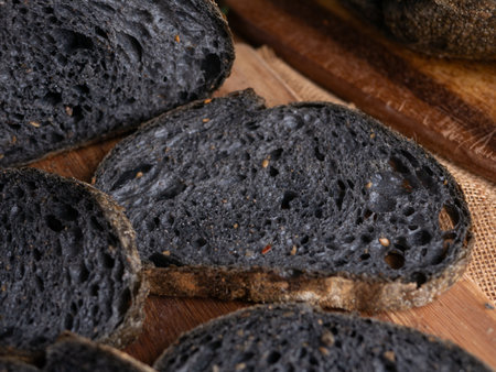 Fresh baked black charcoal sourdough ciabatta bread sliced on wooden boardの写真素材