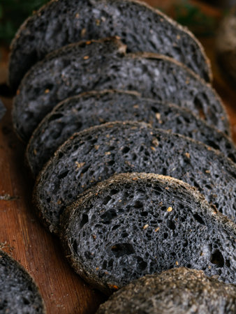 Fresh baked black charcoal sourdough ciabatta bread sliced on wooden boardの写真素材