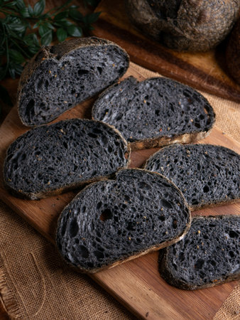 Fresh baked black charcoal sourdough ciabatta bread sliced on wooden board