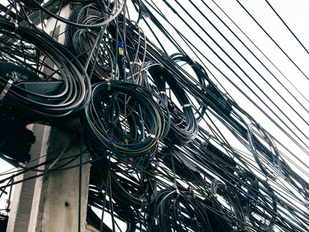 Messy tangled overhead cable wires on utility pole in urban city infrastructure.
