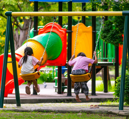 Happy young girl swinging on playground swing having fun in public park with lush green trees - joyful childhood recreation and outdoor play activity.の写真素材