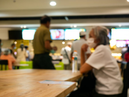 Elderly person sitting at table in food court or cafeteria at hospital, shopping mall, school or university - senior citizen dining and social interaction.の写真素材