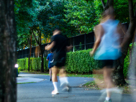 Blurred Motion Runners Jogging on Tree-Lined Street Path in Residential Area - Dynamic Exercise Movement.の写真素材