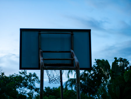 Basketball Hoop and Net Against Blue Sky with Green Trees - Outdoor Sport Court in Twilight.の写真素材