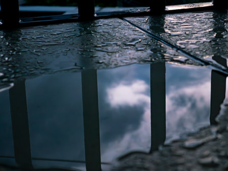 Metal Fence Reflection in Water Puddle - Abstract Mirror Effect with Iron Railing and Cloudy Sky