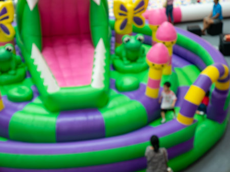 Blurred green inflatable playground bounce house slide with children playing at indoor amusement entertainment center.の写真素材