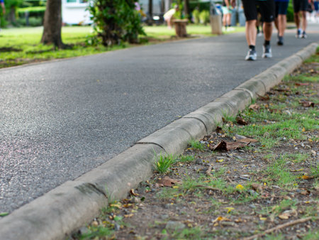 Close-up Concrete Curb with Runners and Walkers Exercising on Park Path - Urban Fitness Perspective.の写真素材