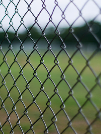 Close-Up of Chain Link Fence with Shallow Depth of Field - Metal Wire Mesh Barrier with Blurred Green Backgroundの写真素材