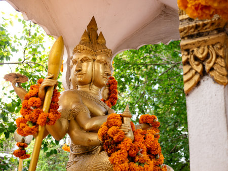 Golden Four-Faced Brahma Statue Adorned with Orange Marigold Flower Garlands at Hindu Buddhist Shrineの写真素材