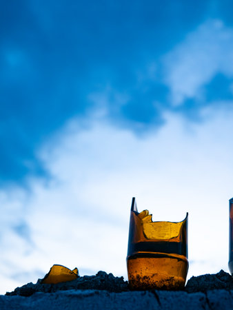 Broken Glass Bottles Embedded in Concrete Wall Against Blue Sky - Security Barrier and Urban Defense Systemの写真素材
