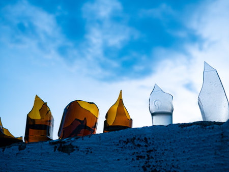 Broken Glass Bottles Embedded in Concrete Wall Against Blue Sky - Security Barrier and Urban Defense Systemの写真素材