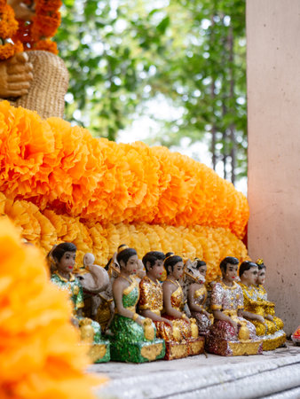 Traditional Thai Angel Figurines with Orange Marigold Garlands at Buddhist Shrine - Handcrafted Religious Offeringsの写真素材