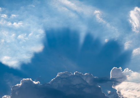 Dramatic sunbeams breaking through white cumulus clouds in deep blue sky creating crepuscular raysの写真素材