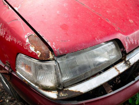 Severe rust corrosion and peeling paint damage on red car hood edge above headlight showing metal deteriorationの写真素材