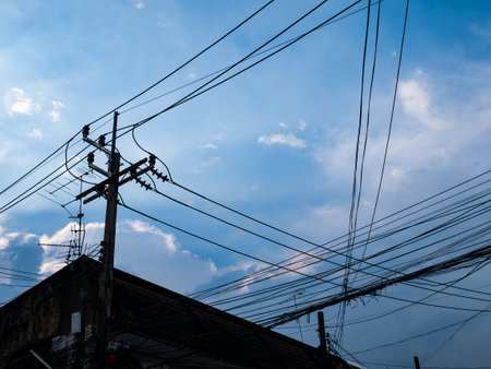 Dramatic blue sky with white cumulus clouds and electric power lines crossing diagonally in urban settingの写真素材
