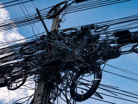 Messy tangled electrical power cables and wires on utility pole against blue sky showing chaotic infrastructureの写真素材