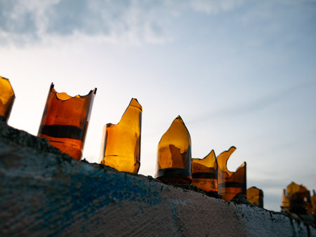 Row of Broken Amber Glass Bottles on Wall Against Dramatic Evening Sky - Traditional Security Barrier Silhouetteの写真素材
