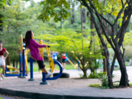 Children playing on spring rider toy in public park with blurred people exercising in backgroundの写真素材