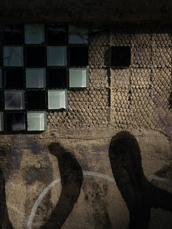 Broken dirty glass block window tiles falling off deteriorated wall with dramatic shadows on concrete groundの写真素材