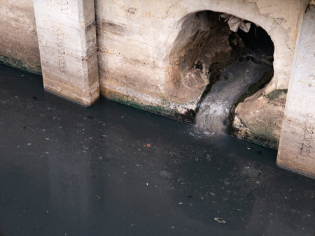 Dirty Polluted Wastewater Flowing from Old Concrete Drainage Pipe into Dark Canalの写真素材