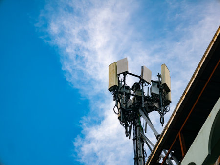 Cellular telecommunications tower with antennas and equipment against blue sky with white clouds and power linesの写真素材
