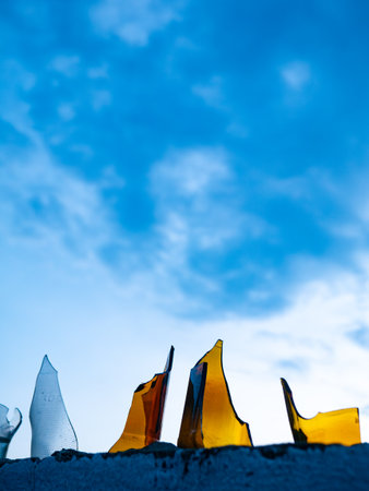 Broken Glass Bottles Embedded in Concrete Wall Against Blue Sky - Security Barrier and Urban Defense Systemの写真素材