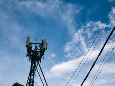 Cellular telecommunications tower with antennas and equipment against blue sky with white clouds and...