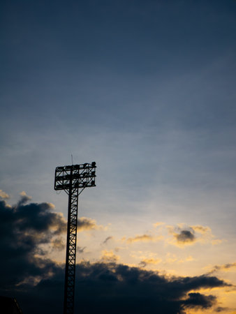 Silhouette of Stadium Floodlight Tower Against Dramatic Sunset Sky with Golden Clouds at Dusk