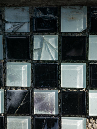 Old dirty cracked glass block tiles in black and white checkered pattern with scratches and...