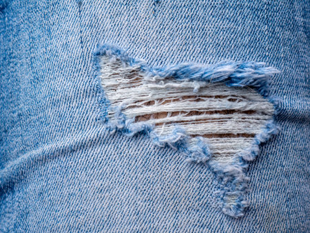 Ripped Torn Blue Jeans Denim Fabric Texture Close-Up Showing Frayed Threads and Skin