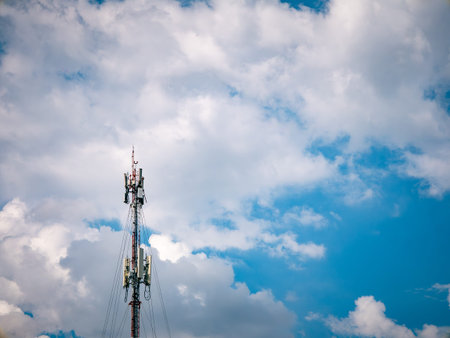 Tall telecommunication antenna tower against a bright blue sky and white clouds, mobile network and...