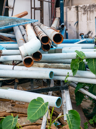 Stack of Used White and Blue PVC Pipes with Rusty Metal Pipes