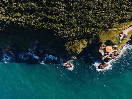 Aerial shot of cliff with lighthouse on the ledge and the ocean hitting the rocksの写真素材