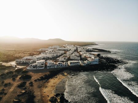 Aerial shot of village in Famara, Canary islands with ocean waves and beach at sunsetの写真素材