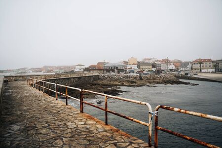 Misty fishing village in Galicia, Spain with rocky coastline and rusty harbourの写真素材