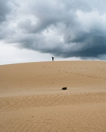 Man walking on top of desert dune with cloudy sky in Canary Islands, Spainの写真素材