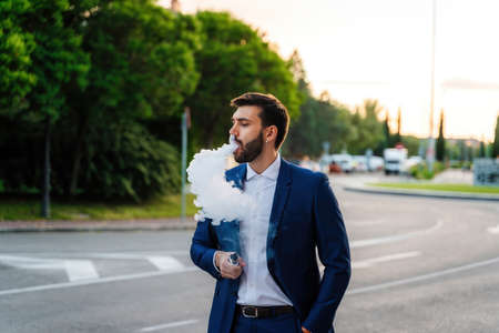 Young elegant business man with surgical mask looks at phone in parkの写真素材