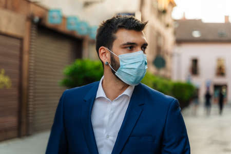 Young elegant business man with surgical mask looks at phone in parkの写真素材