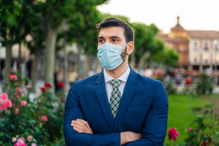 Young elegant business man with surgical mask looks at phone in parkの写真素材