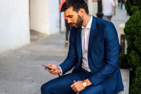 Young elegant business man with surgical mask looks at phone in park